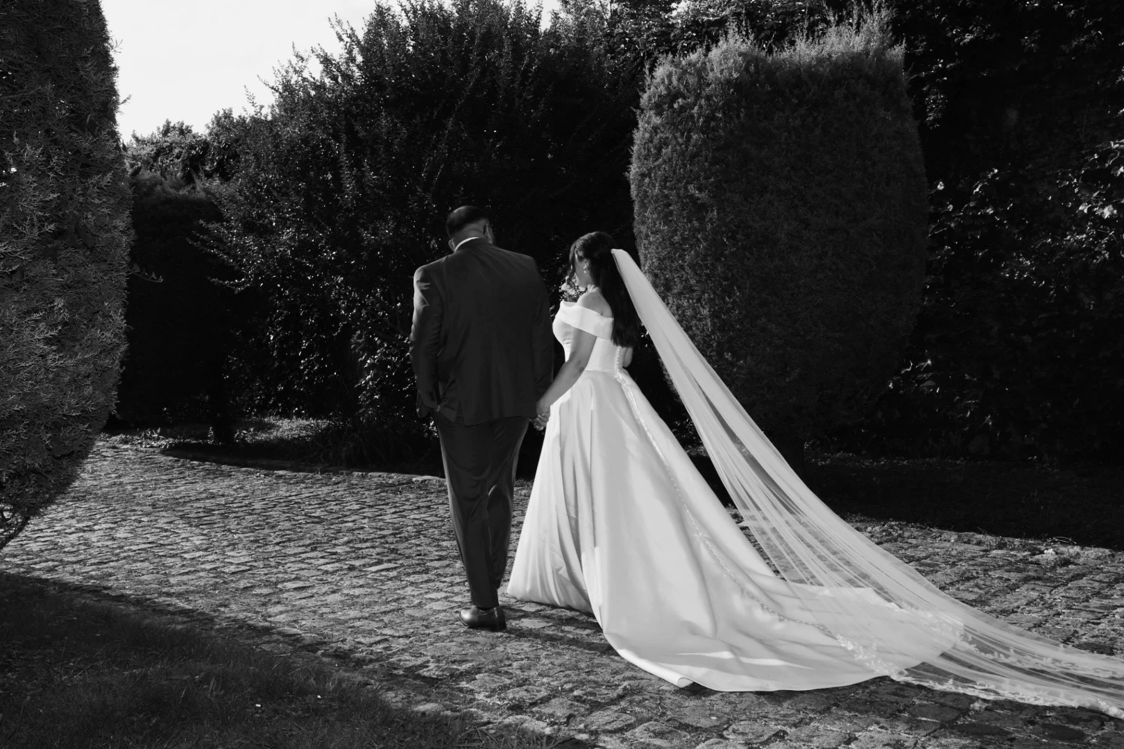 Les mariés de dos dans une allée de jardin, en noir et blanc