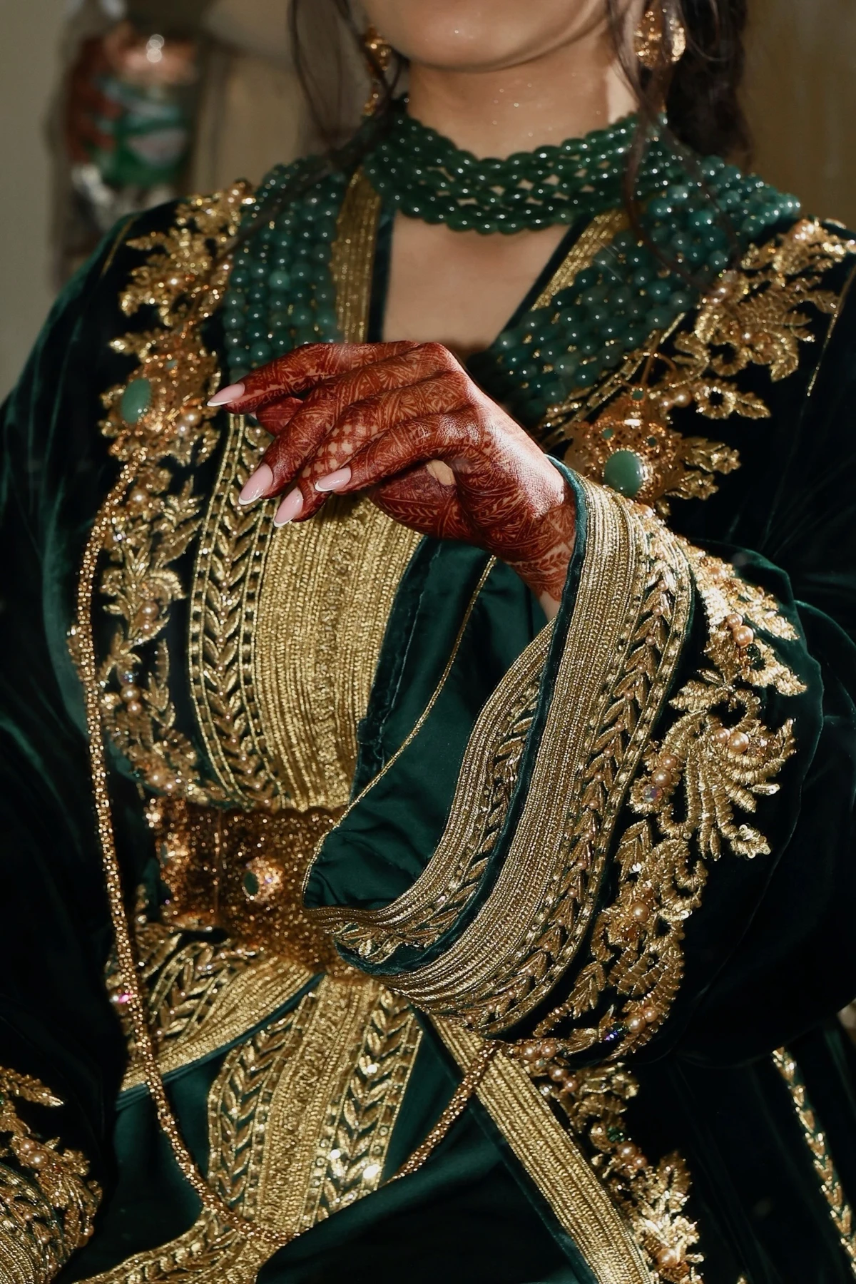Détails de tenue marocaine verte et dorée, bijoux et mains ornées de henné